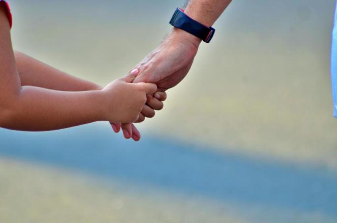 Kind hält die Hand eines Erwachsenen.