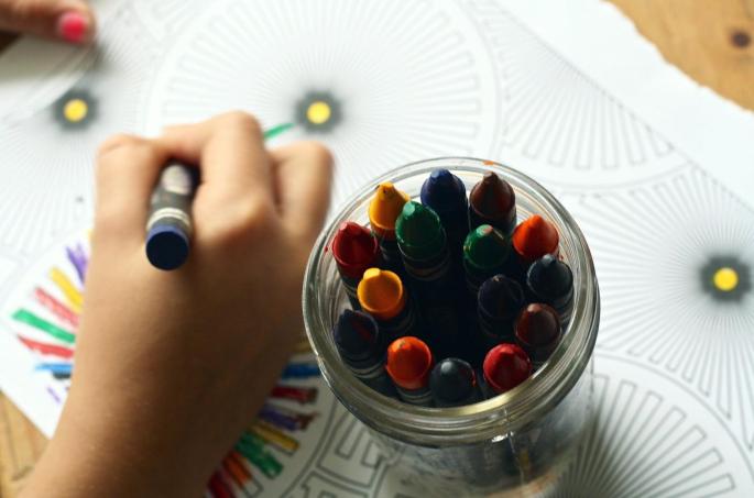 Die Hand eines Kindes, dass mit Bundstiften malt sowie ein Glas voll mit Bundstiften.