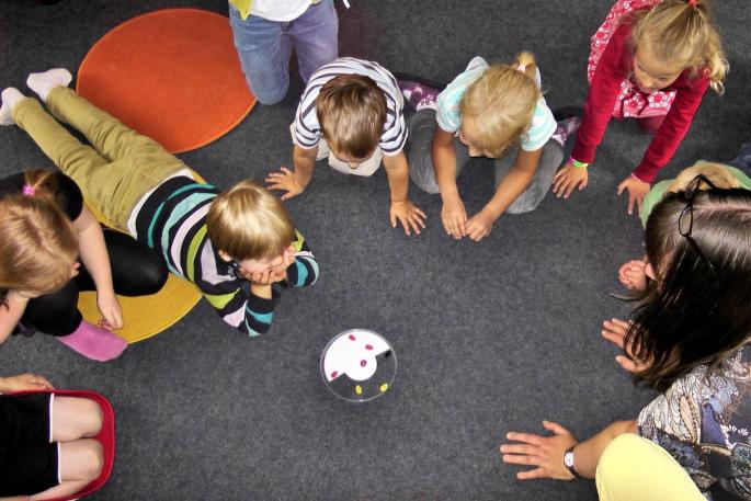 Kinder, die im Kreis sitzen bzw. liegen und auf ein Spielzeug schauen.