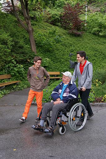 Zwei junge Menschen mit einem alten Mann im Rollstuhl.