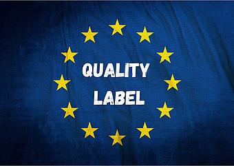 Blaue EU-Flagge mit gelben Sternen. In der Mitte stehen die Wörter Quality Label in weißer Schrift geschrieben.