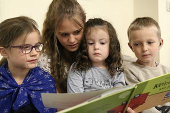 Eine Frau liest drei Kindern ein Buch vor.