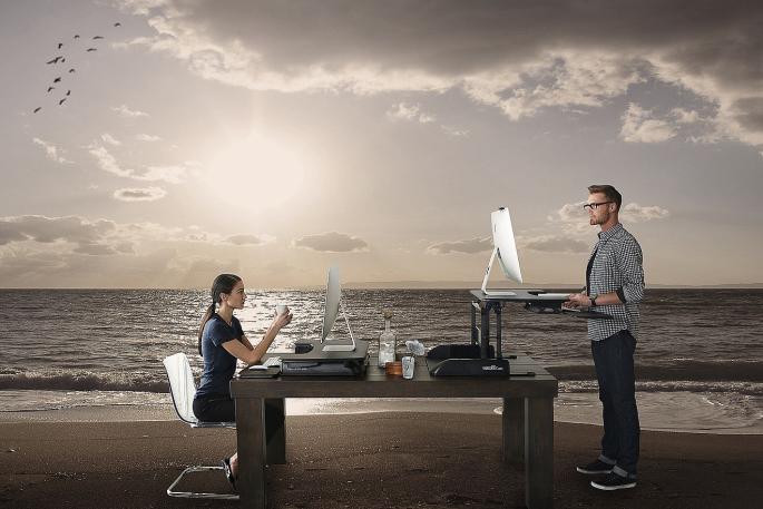 Zwei Menschen am Schreibtisch am Strand eines Meeres. Die beiden arbeiten.