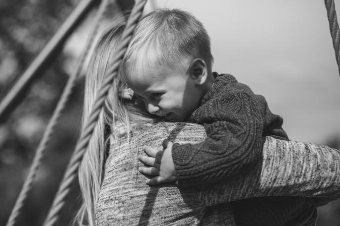 Ein Kleinkind in den Armen seiner Mutter. Bild ist in schwarz weiß.