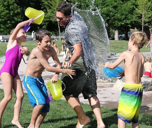 Spielspaß von Kindern mit einem Erwachsenen im Schwimmbad. Die Kinder schütten den Mann mit Wasser aus Kübeln an.