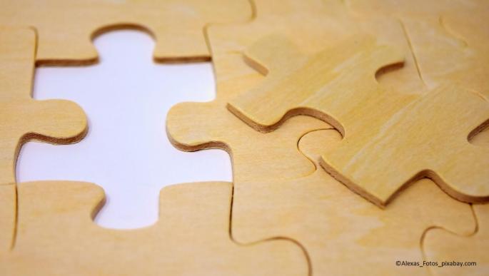Auf dem Bild sieht man Puzzle-Teile aus Holz. Eines wurde herausgenommen und auf die rechte Seite gelegt.