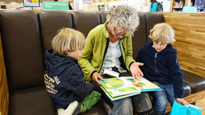 Ältere Dame die mit zwei Kindern ein Buch liest.
