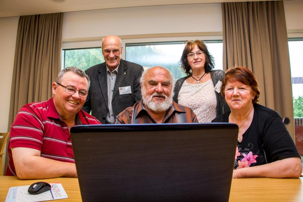 Mehrere ältere Menschen, die gemeinsam in einen Laptop hinein schauen. Bei den Leuten handelt es sich um Mitglieder und Besucher einer Computeria in Tirol.