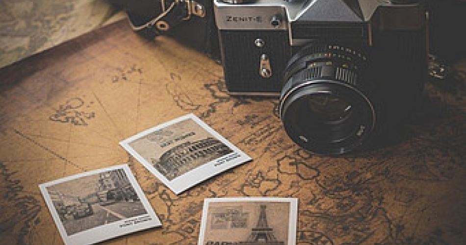 Auf dem Bild sieht man eine Kamera und drei geschossene Polaroidfotos. Die Kamera und die Fotos liegen auf einer braunen Landkarte.