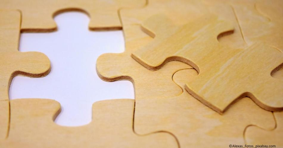 Auf dem Bild sieht man Puzzle-Teile aus Holz. Eines wurde herausgenommen und auf die rechte Seite gelegt.