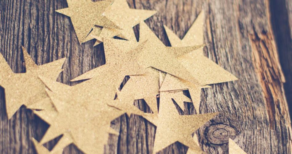 Goldene Sterne aus Papier, die auf einem Holzuntergrund liegen.